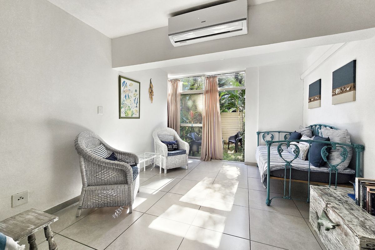 A bright living area featuring tiled flooring, a wall-mounted split-system air conditioner, and large sliding glass doors providing access to the outdoor space.