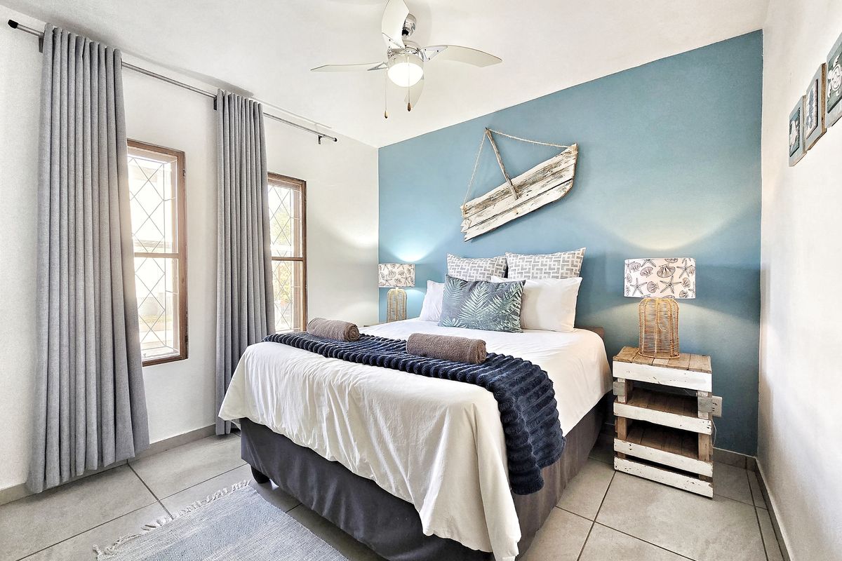 A well-maintained bedroom featuring tiled flooring, a central ceiling fan, and leaded glass windows with floor-to-ceiling curtains.