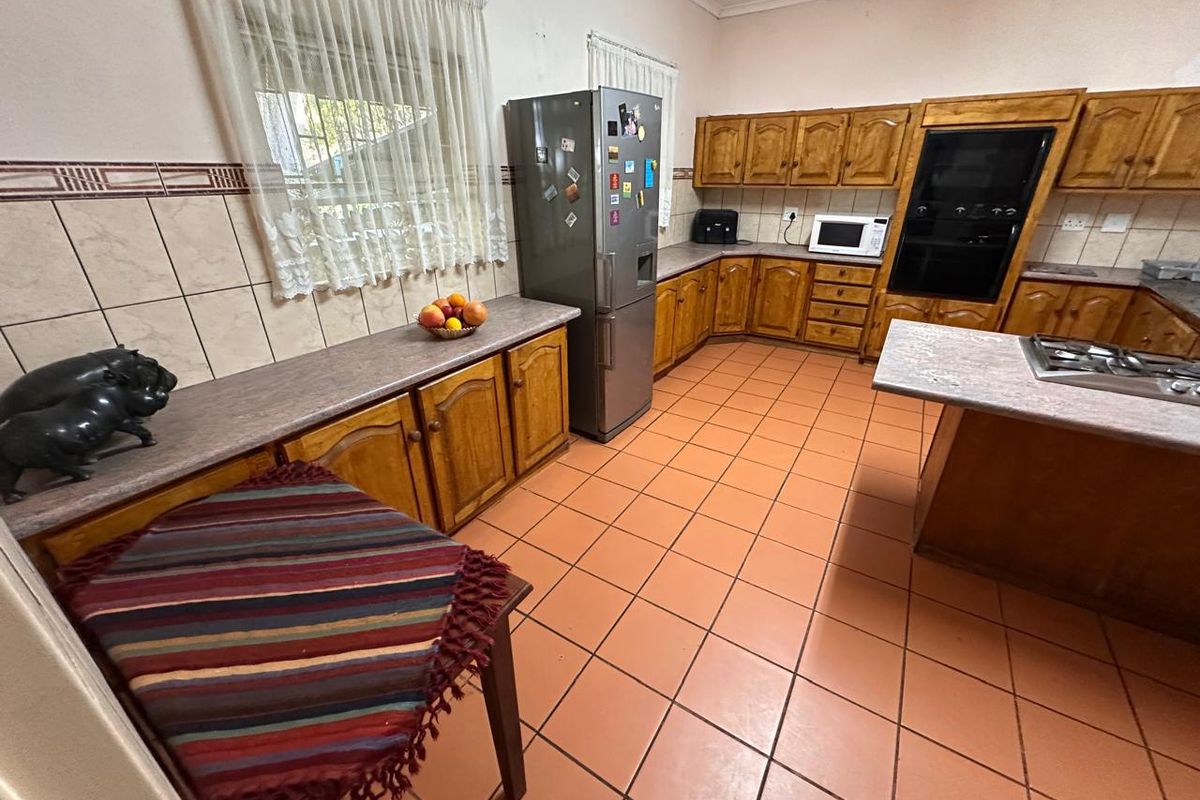 A functional kitchen featuring traditional wooden cabinetry, laminate countertops, built-in oven, gas hob, and ceramic tiled flooring throughout.