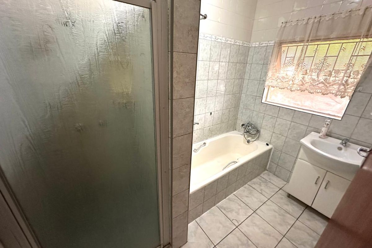 A functional bathroom featuring a separate shower enclosure, built-in bathtub, and a vanity cabinet with tiled walls and flooring.