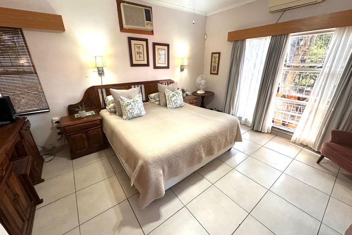 A well-lit bedroom featuring tiled flooring, dual air conditioning units, and large windows with security bars, offering a functional and comfortable living space.
