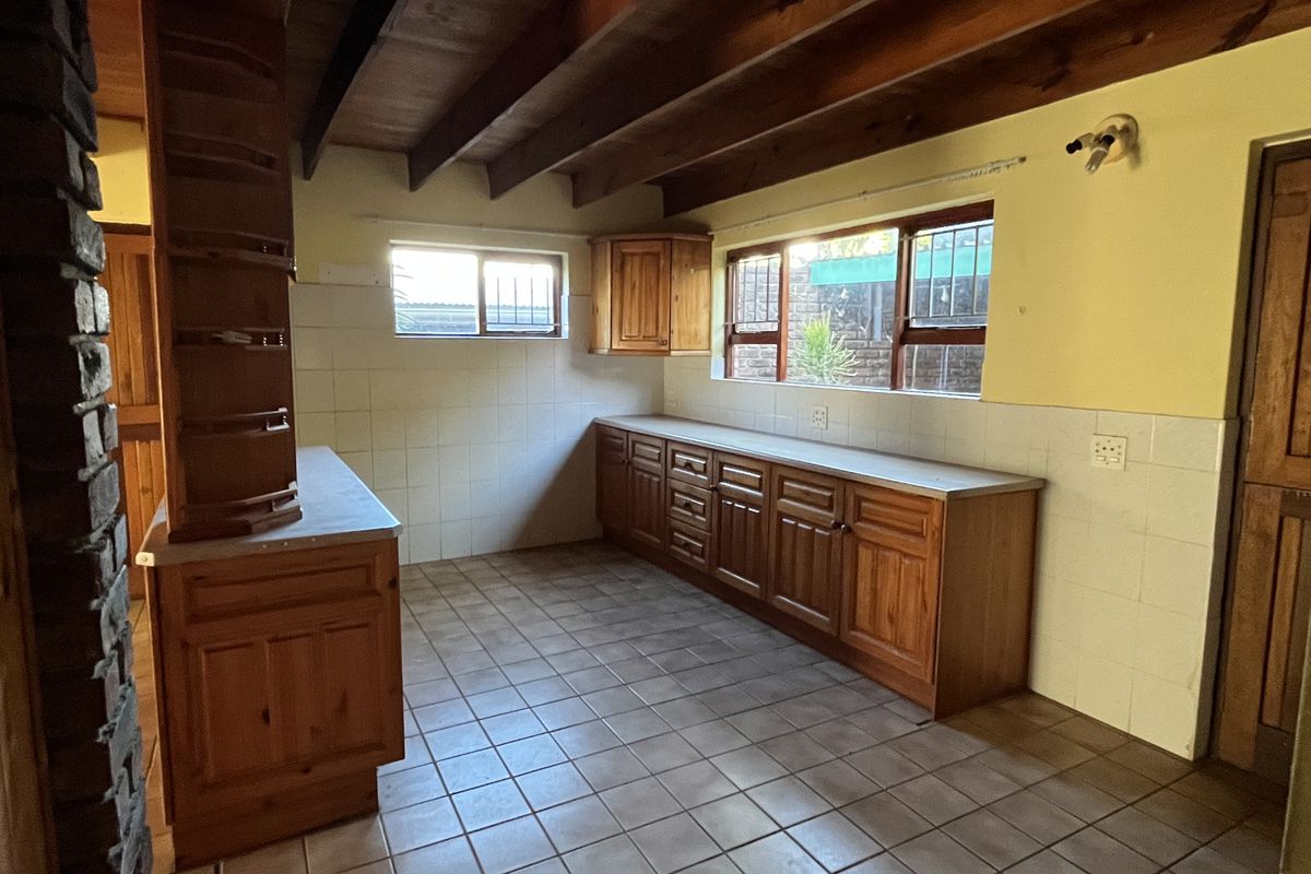 A spacious, empty kitchen featuring traditional wooden cabinetry, exposed timber ceiling beams, and tiled flooring, offering a blank canvas for modern renovation.
