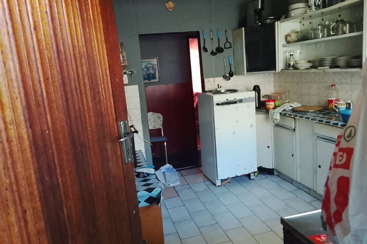A functional kitchen space featuring tiled flooring, wall-mounted cabinetry, and a tiled backsplash, offering potential for modernization and layout optimization.