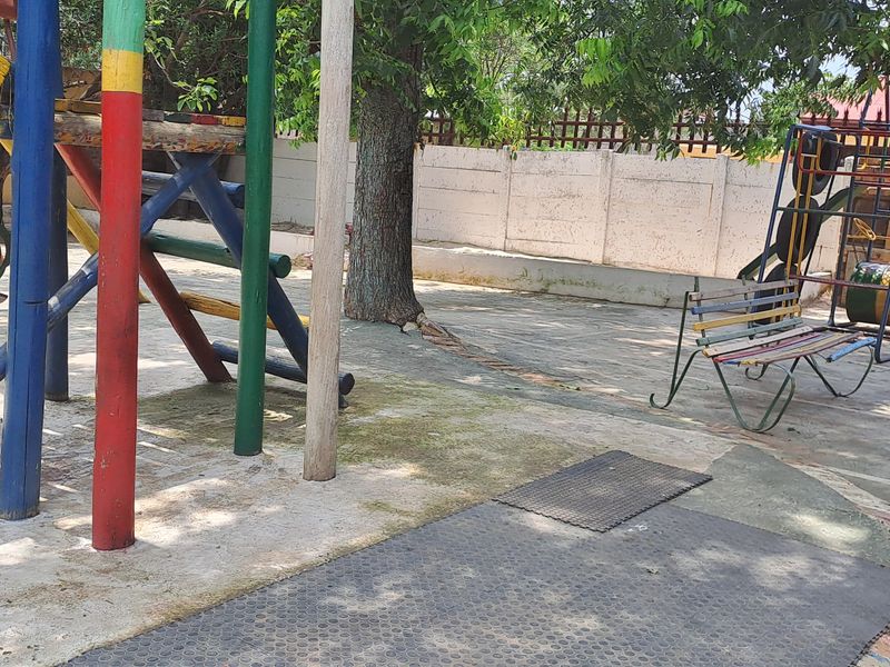 A paved outdoor garden area featuring a concrete boundary wall and mature trees, currently utilized as a play space.