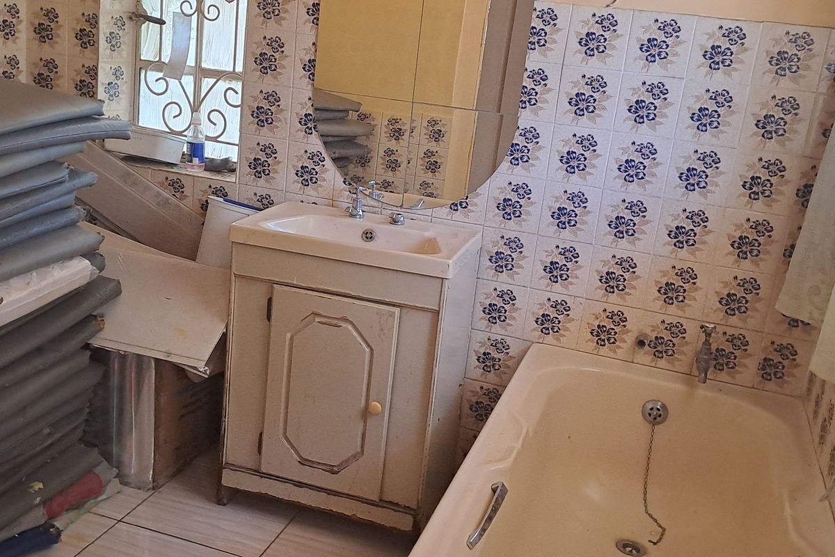 A dated bathroom featuring a vanity cabinet, bathtub, and patterned wall tiles. The space requires modernization to improve its overall aesthetic and functionality.