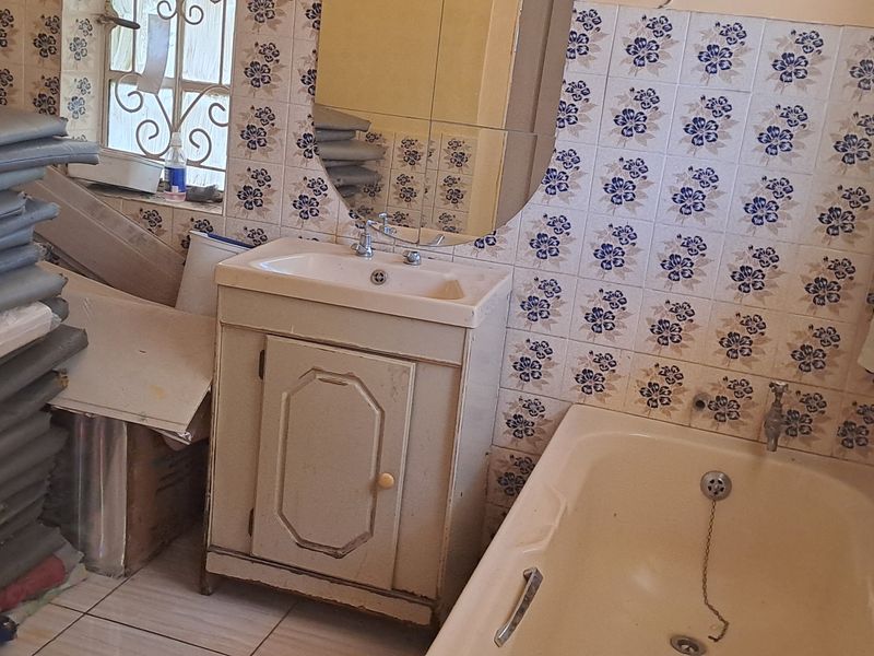 A dated bathroom featuring a vanity cabinet, bathtub, and patterned wall tiles. The space requires modernization to improve its overall aesthetic and functionality.