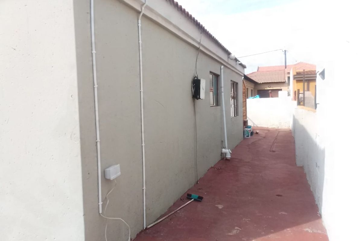 A side exterior view of the property showing painted walls, external conduit piping, and a concrete pathway leading to the rear area.