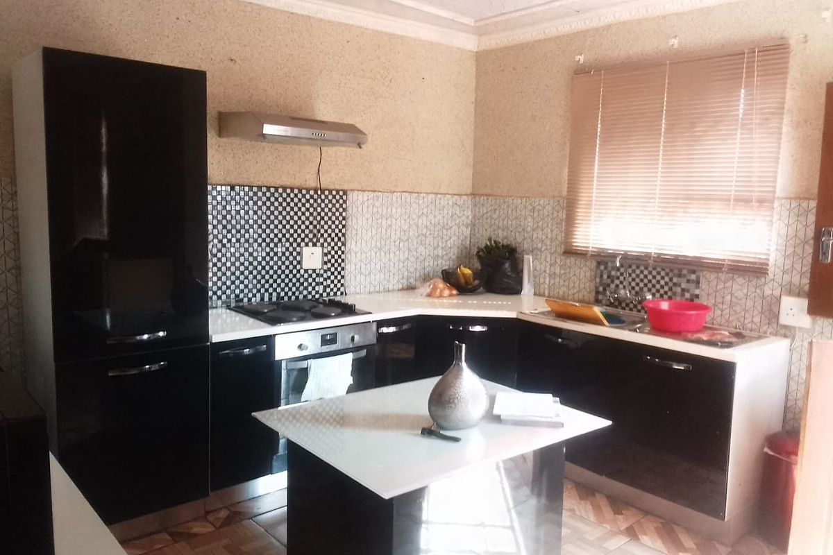 A functional kitchen featuring black cabinetry, a central island, built-in oven and hob, and a tiled backsplash with a window for natural light.