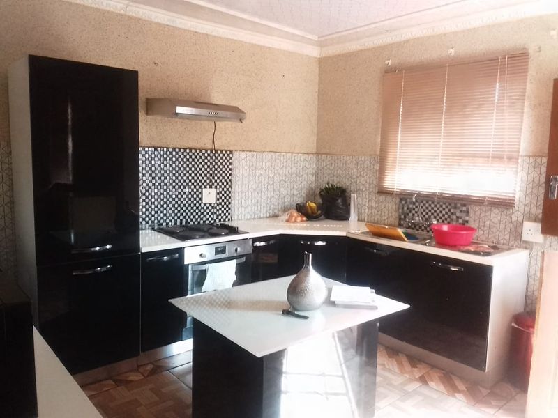 A functional kitchen featuring black cabinetry, a central island, built-in oven and hob, and a tiled backsplash with a window for natural light.