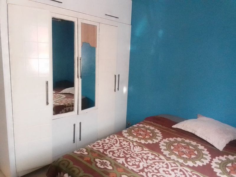 A bedroom featuring a built-in white wardrobe with a damaged mirror panel and blue accent wall.
