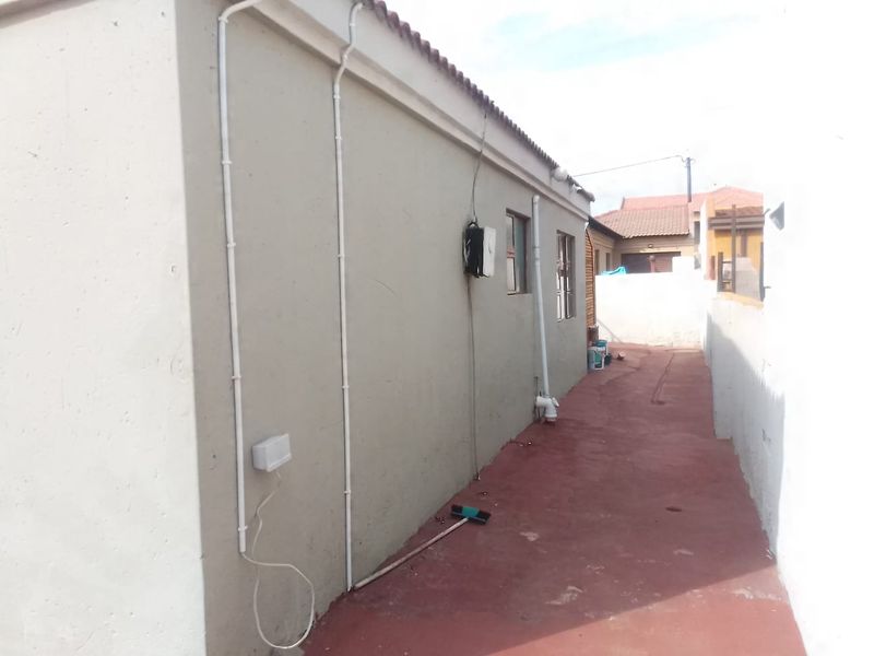 A side exterior view of the property showing painted walls, external conduit piping, and a concrete pathway leading to the rear area.
