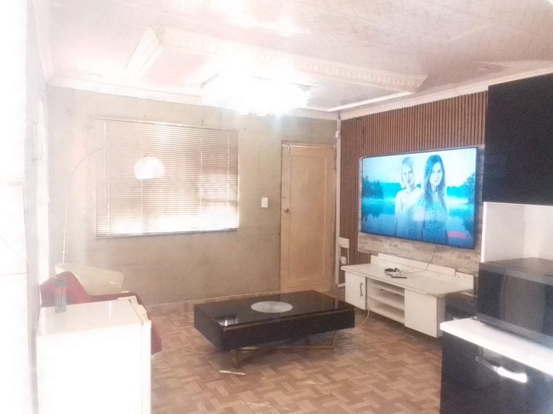 Living room featuring slatted wood wall paneling, decorative ceiling molding, and tiled flooring. The space requires finishing touches to the wall surfaces.
