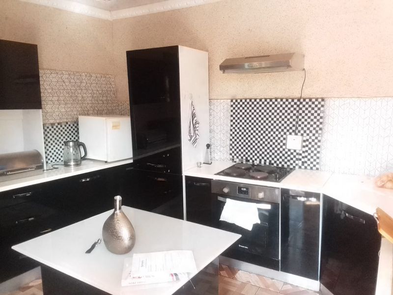 A compact kitchen featuring modern black cabinetry, a built-in oven with electric hob, extractor fan, and contrasting geometric tiled splashbacks.