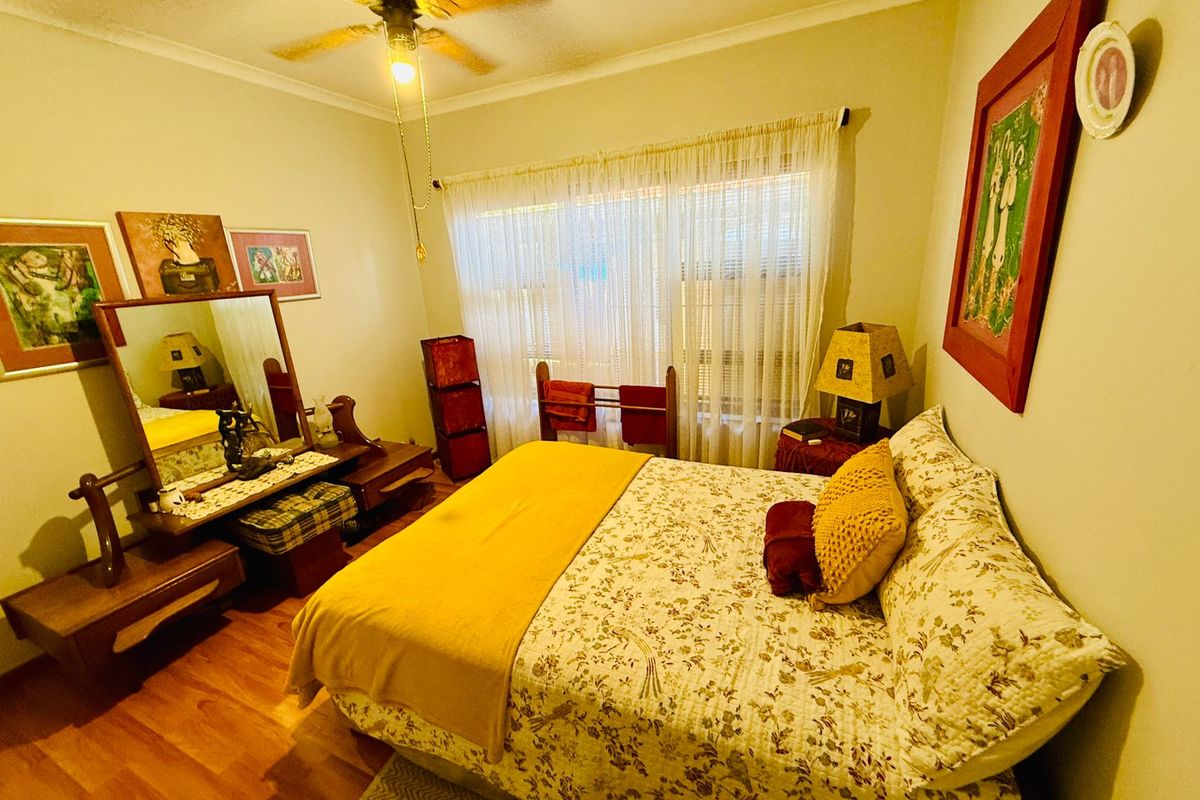A cozy bedroom featuring wood-look flooring, a ceiling fan, and a large window with sheer curtains, providing a comfortable and functional living space.