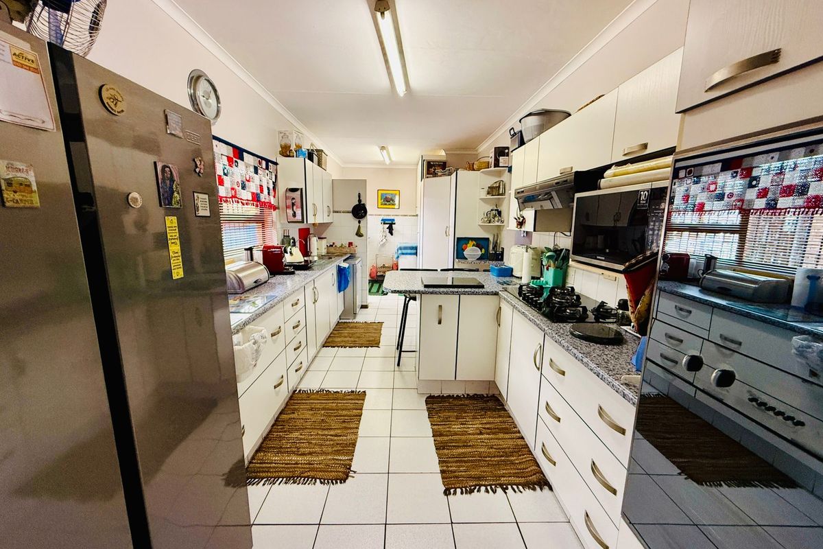 A functional galley-style kitchen featuring laminate cabinetry, granite-look countertops, a built-in gas hob, and tiled flooring.