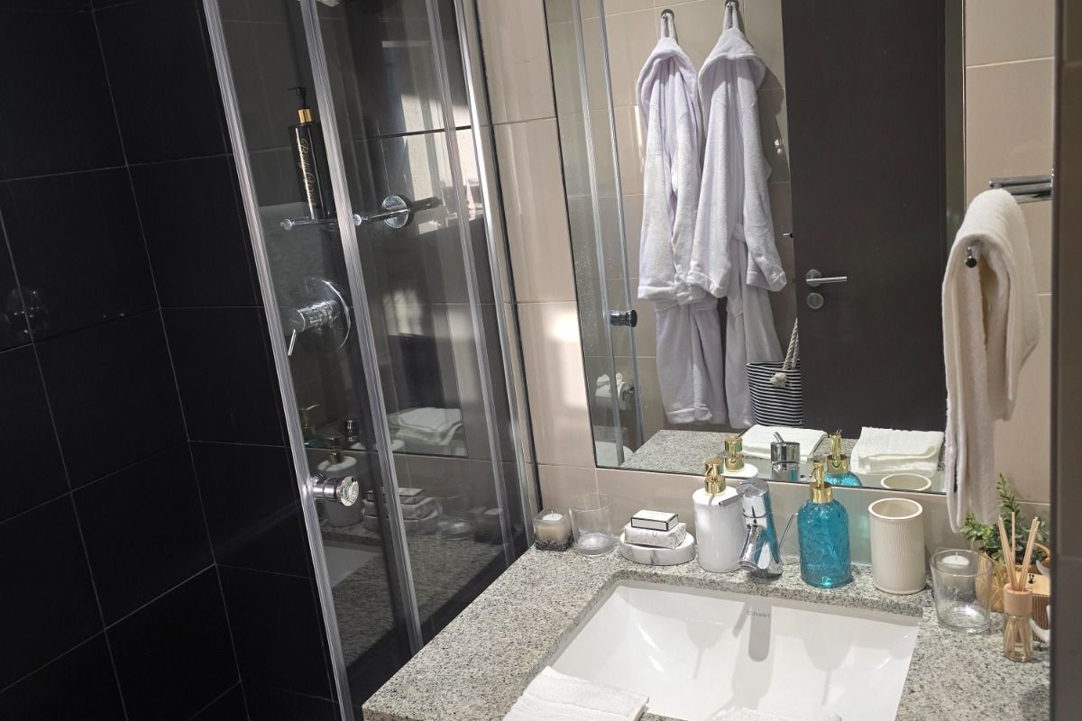 Modern bathroom featuring a glass-enclosed shower, granite vanity countertop with undermount sink, and large wall-mounted mirror with neutral and black tiled finishes.