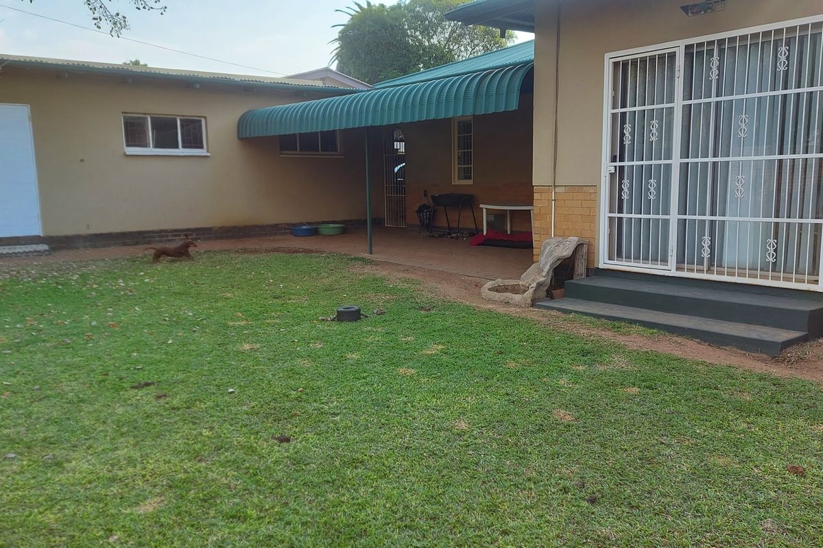 Rear view of the property featuring a covered patio area, security gates, and a private lawn space.