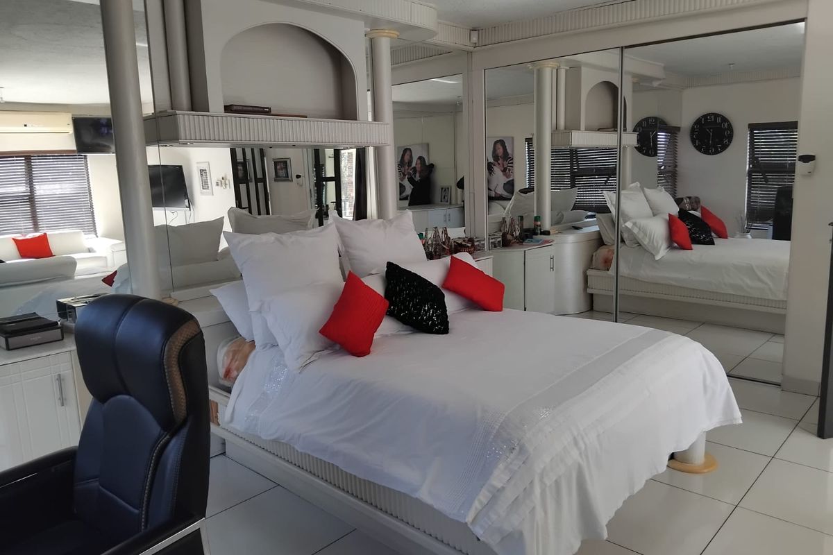 Spacious bedroom featuring extensive mirrored wall paneling, tiled flooring, and built-in cabinetry with integrated lighting elements.