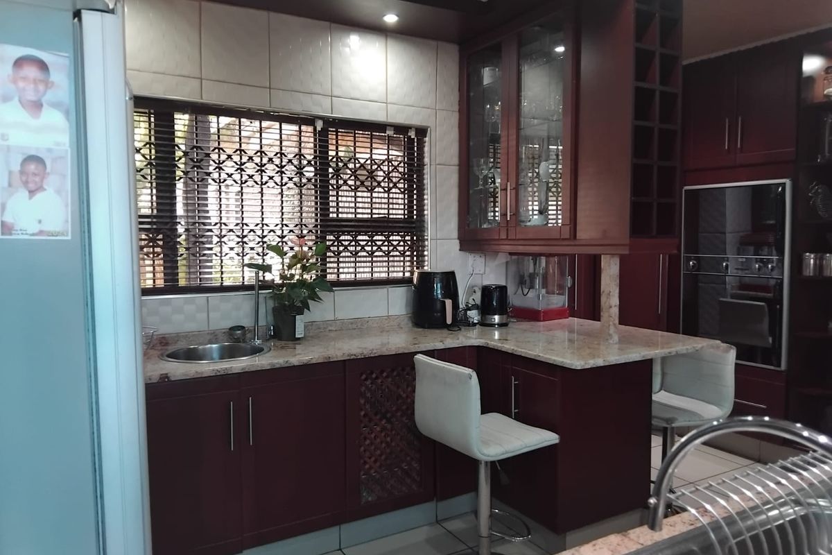 A functional kitchen featuring dark wood cabinetry, granite countertops, a built-in oven, and a breakfast bar area with tiled flooring.