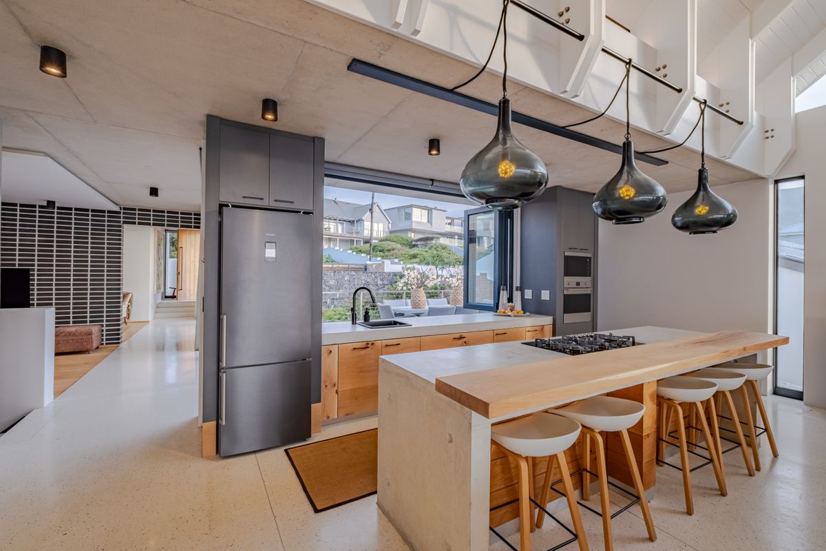 Modern open-plan kitchen featuring a concrete island with breakfast bar, high-end built-in appliances, sleek cabinetry, and polished terrazzo flooring.