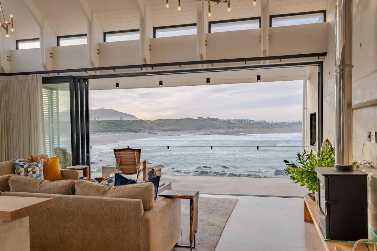Spacious living area featuring vaulted ceilings, exposed rafters, and expansive bi-fold doors opening to a stunning ocean view and private balcony.