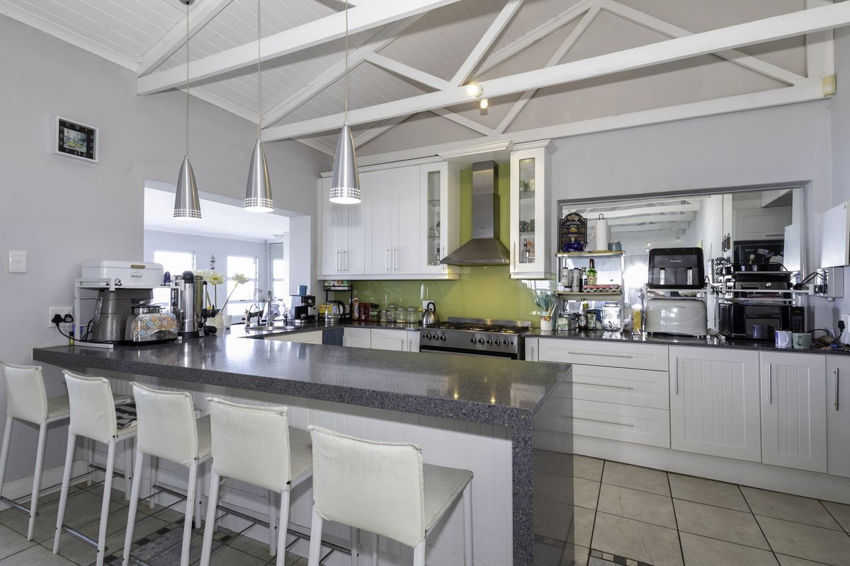 A well-lit kitchen featuring white cabinetry, stone countertops, a central island with breakfast bar seating, and exposed timber trusses on the ceiling.