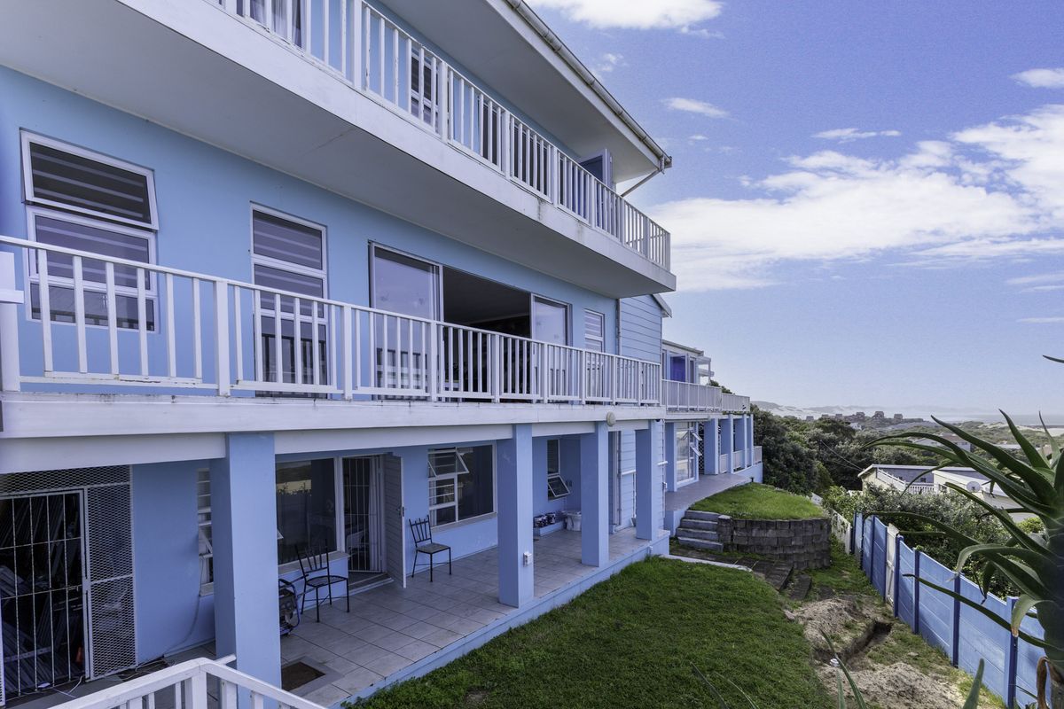 Rear elevation of a multi-story house featuring tiered balconies, sliding glass doors, a covered patio area, and a landscaped garden with retaining walls.