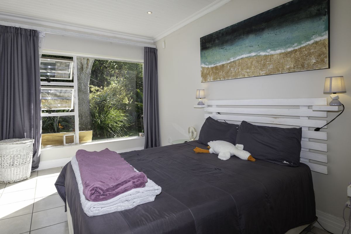A bright and well-maintained bedroom featuring large windows with garden views, tiled flooring, and elegant crown molding.
