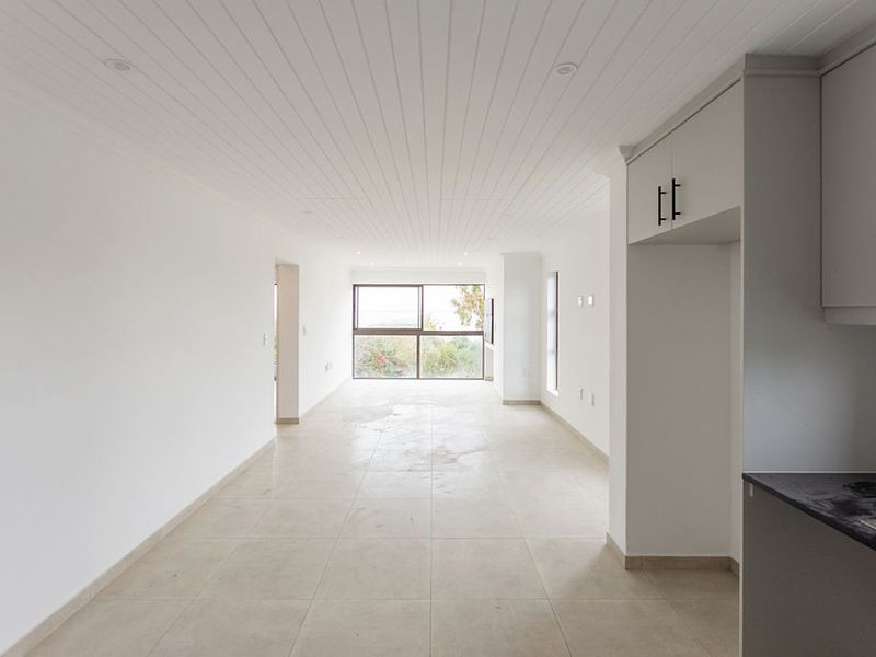 An open-plan living and kitchen area featuring tiled floors, a tongue and groove ceiling, and neutral cabinetry, offering a bright and versatile living space.