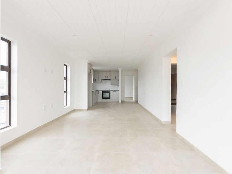 A bright, modern open-plan living and kitchen area featuring neutral tiled floors, clean white walls, and contemporary built-in cabinetry with integrated appliances.
