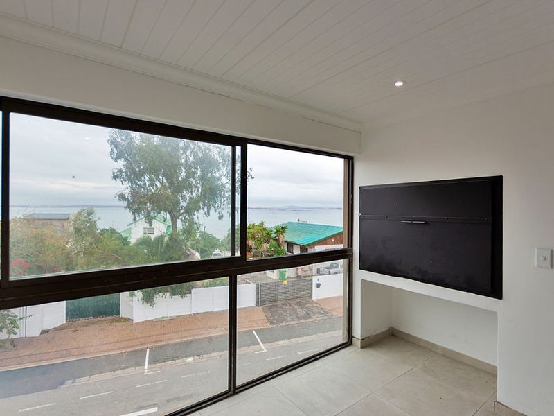An enclosed balcony featuring a built-in braai, large sliding windows with coastal views, and neutral tiled flooring.