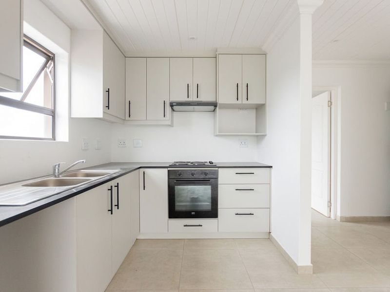 A clean, modern kitchen featuring neutral cabinetry, built-in oven, gas hob, extractor fan, and tiled flooring, offering a bright and functional workspace.