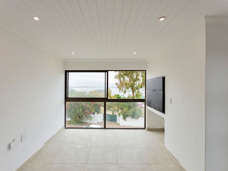 A bright, empty living area featuring tiled floors, a tongue and groove ceiling with recessed lighting, and a large window with scenic views.