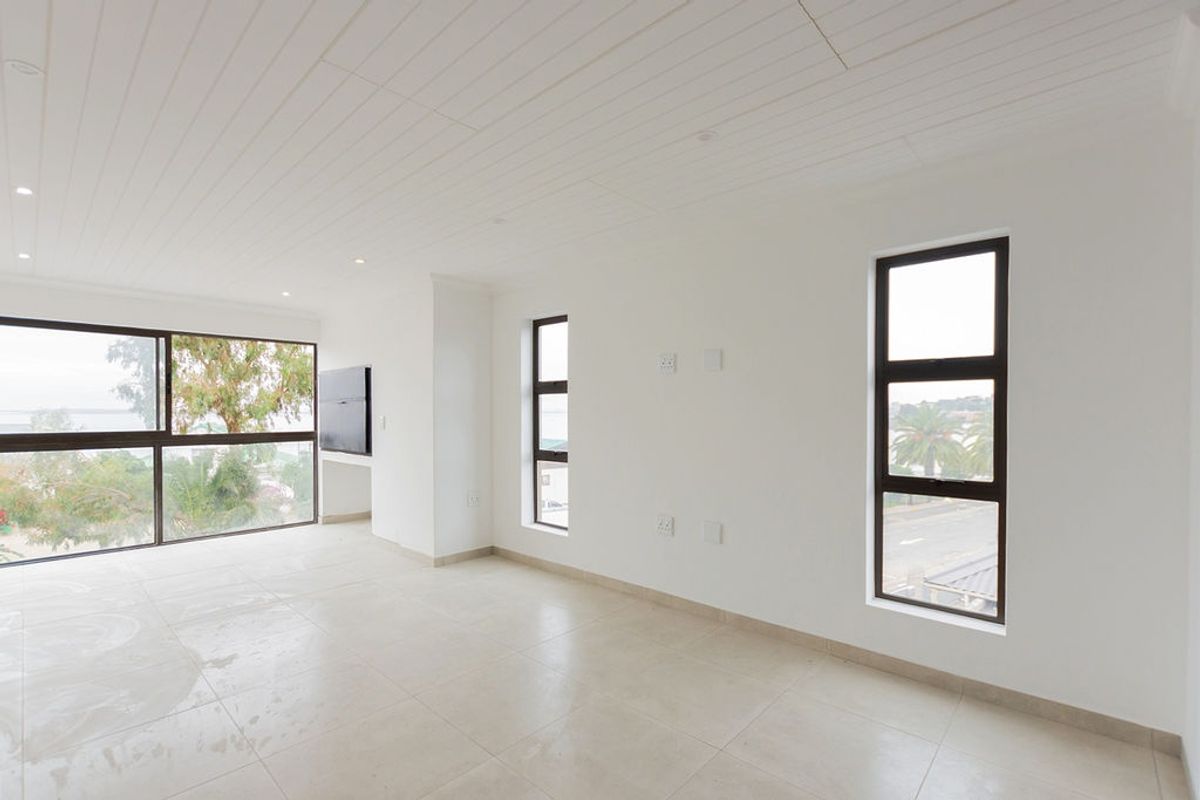 A bright, empty living area featuring tiled floors, a tongue and groove ceiling, and large aluminium-framed windows with views.