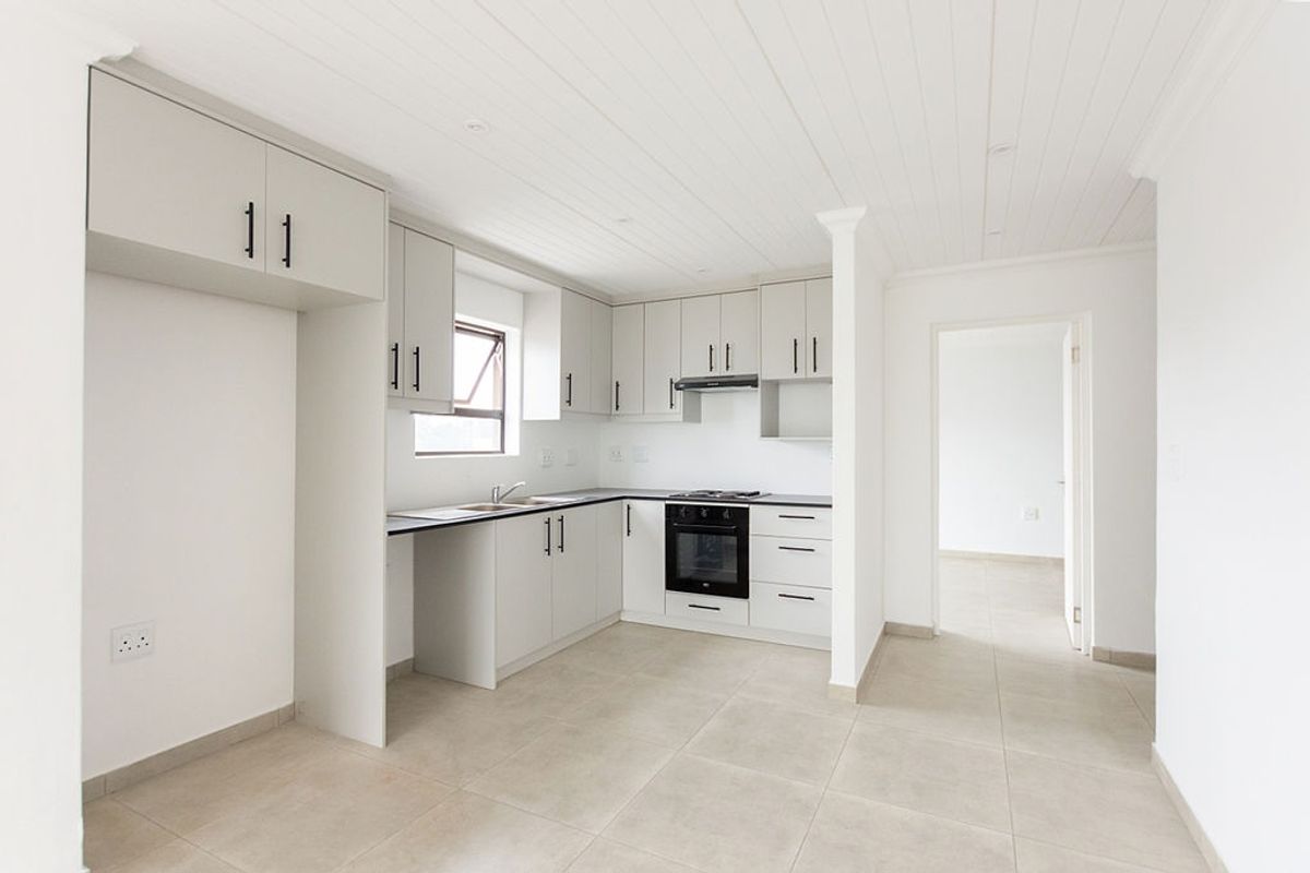 A clean, modern kitchen featuring light-toned cabinetry, built-in oven and hob, tiled flooring, and a white tongue and groove ceiling.
