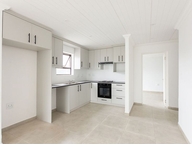 A clean, modern kitchen featuring light-toned cabinetry, built-in oven and hob, tiled flooring, and a white tongue and groove ceiling.