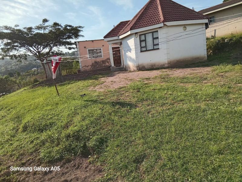 Front view of a detached house featuring a tiled roof and white exterior walls, situated on a sloped grass plot.