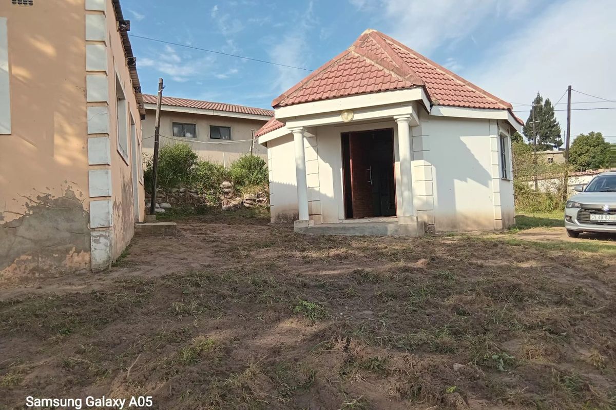 Rear view of the property showing a detached structure with a tiled roof and concrete columns, set within an unlandscaped yard area.