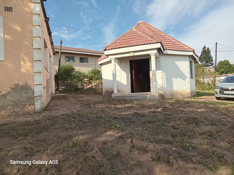 Rear view of the property showing a detached structure with a tiled roof and concrete columns, set within an unlandscaped yard area.