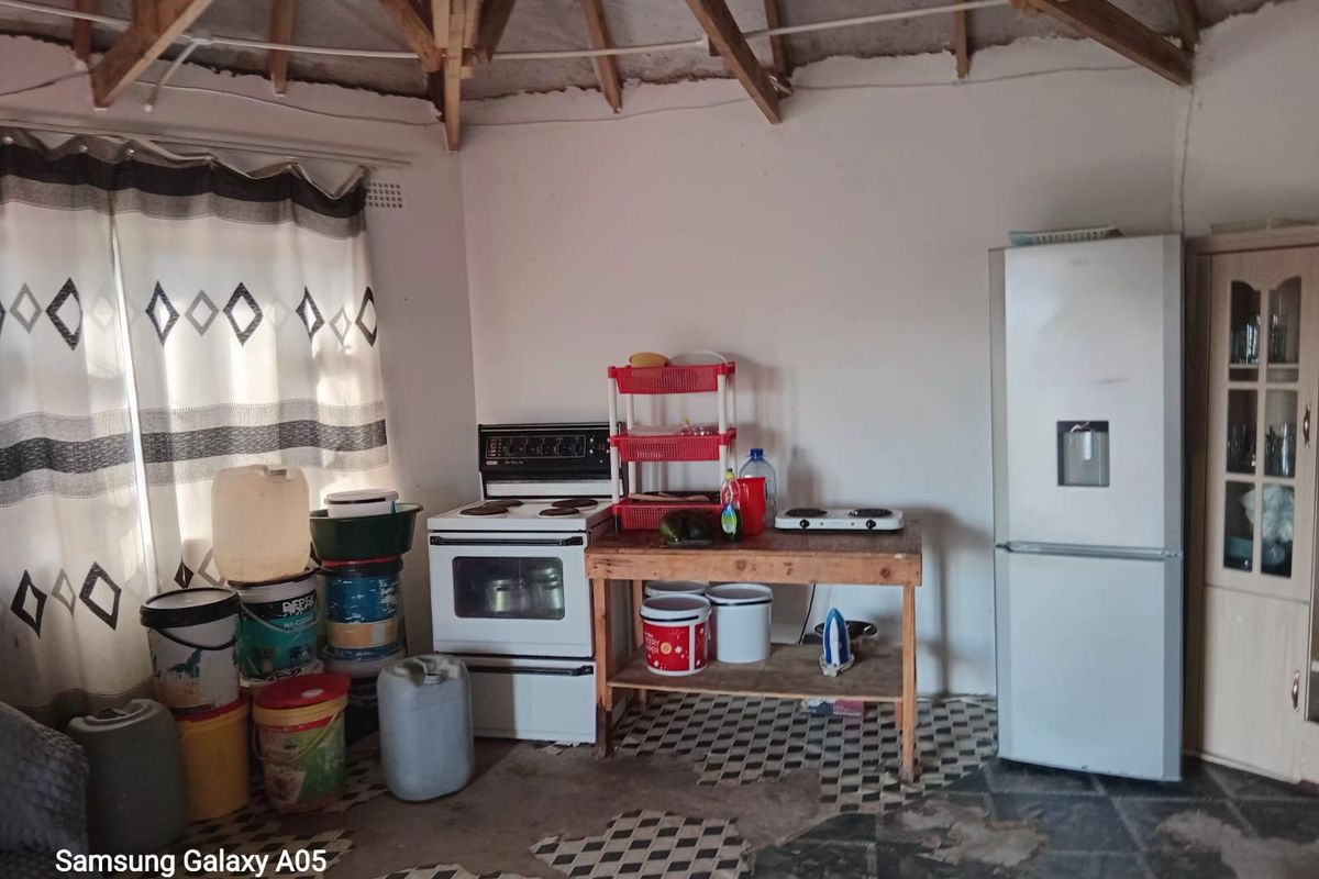 A rustic kitchen area featuring exposed timber roof trusses, a freestanding stove, and significant wear to the floor tiling and wall finishes.