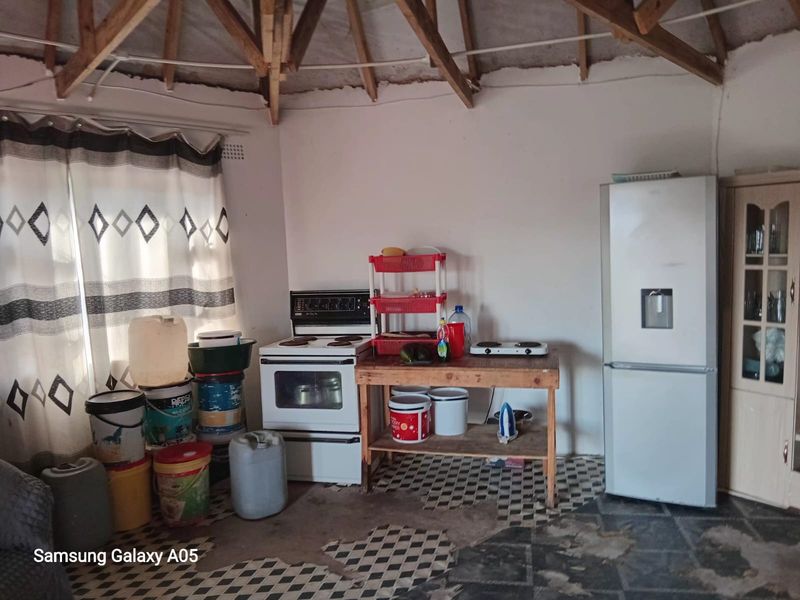 A rustic kitchen area featuring exposed timber roof trusses, a freestanding stove, and significant wear to the floor tiling and wall finishes.