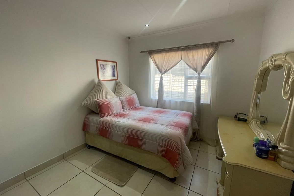 A functional bedroom featuring tiled flooring and a window with curtain rod, providing a simple and practical living space.