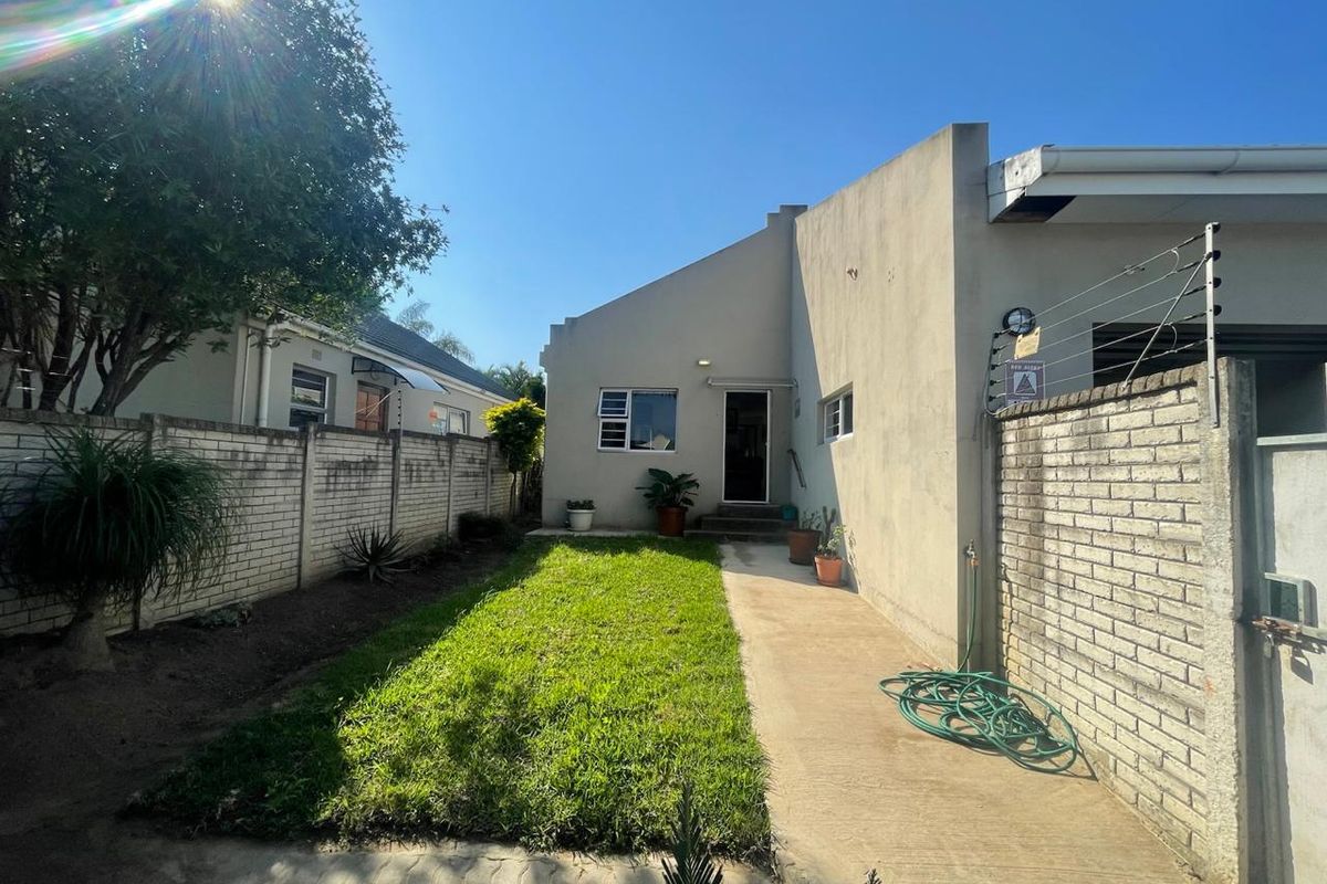 A private rear garden area featuring a concrete pathway, a small lawn, and perimeter brick boundary walls with security fencing.