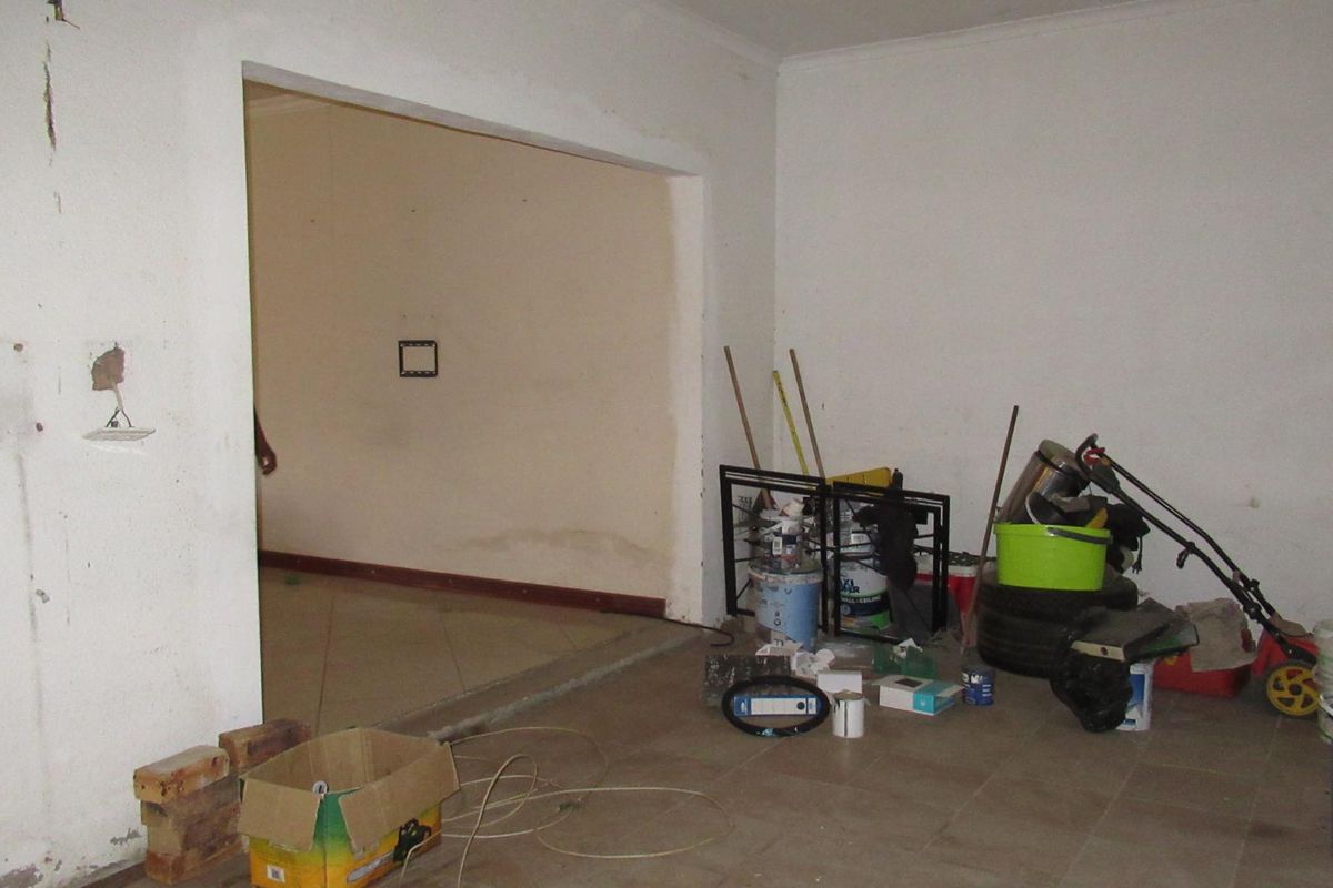 An empty living area featuring tiled flooring and an archway, currently in need of cosmetic repairs and finishing.
