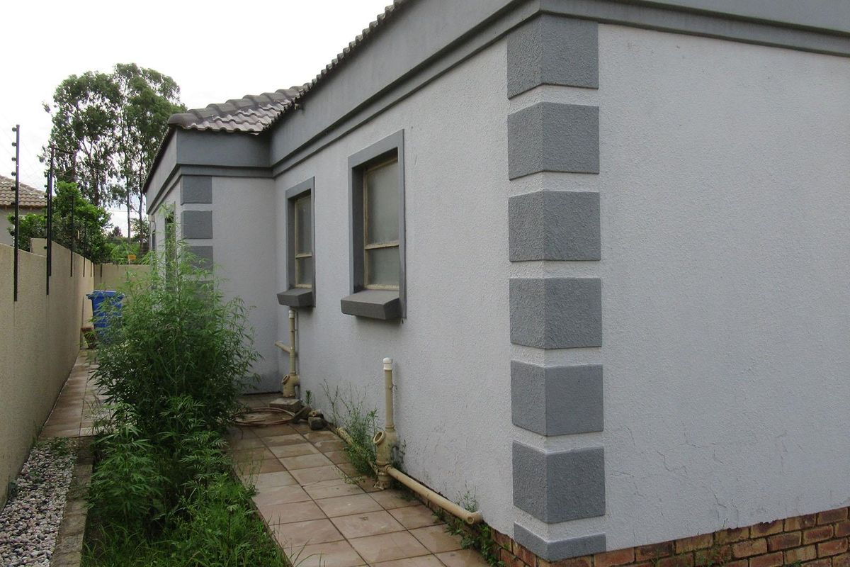 A view of the side exterior of the house featuring a tiled pathway, exposed plumbing, and a perimeter wall with electric fencing.