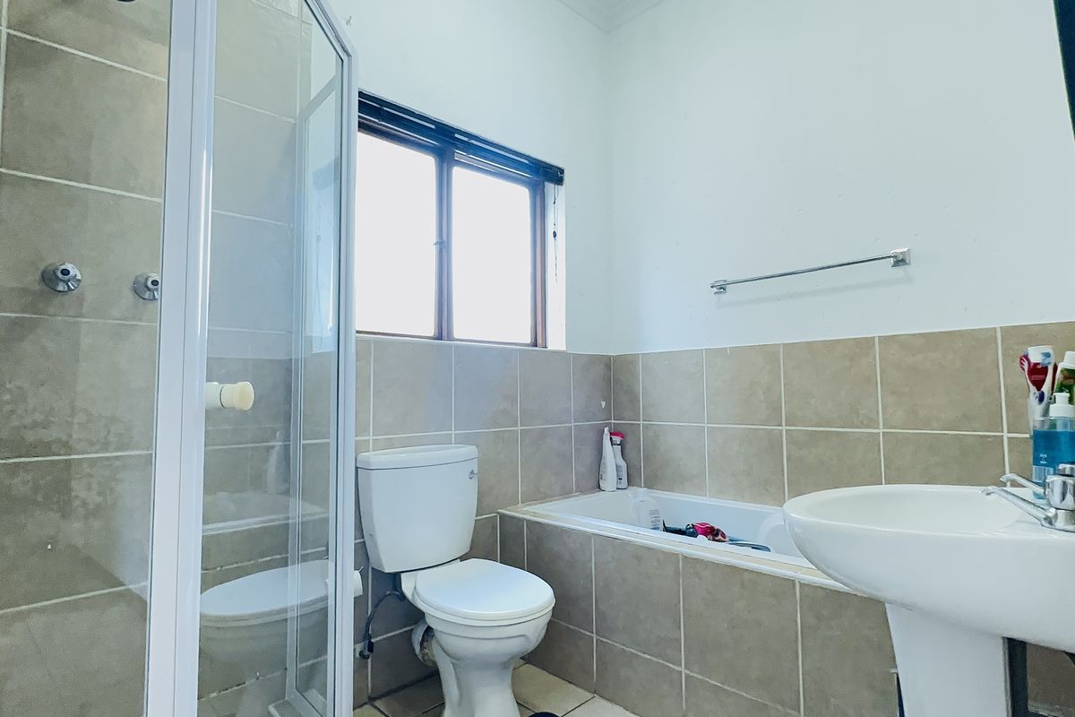 A functional bathroom featuring a shower enclosure, bathtub, pedestal basin, and toilet with neutral wall and floor tiling.
