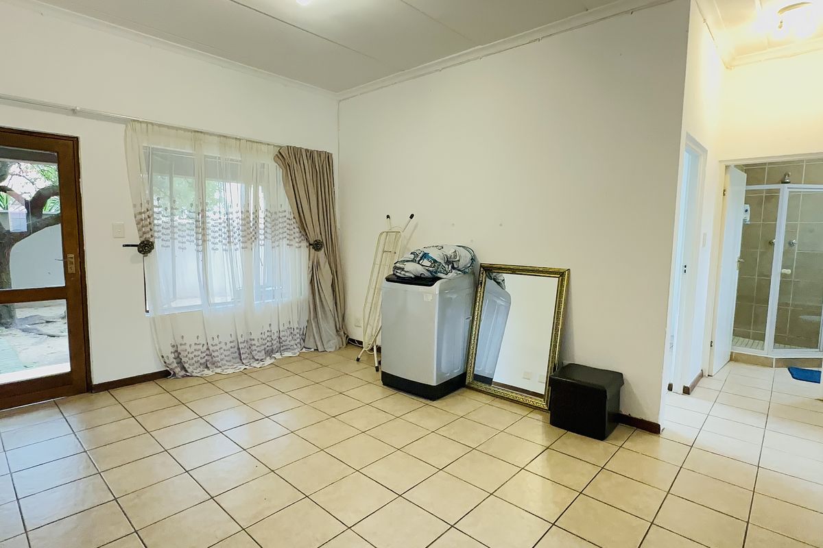 Spacious living area featuring neutral tiled flooring, large windows for natural light, and direct access to an outdoor area, with an adjacent bathroom visible.