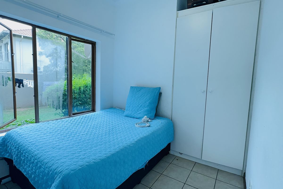 A functional bedroom featuring tiled flooring, a built-in wardrobe, and a large window providing natural light and garden views.
