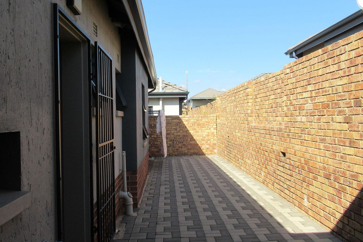 A side exterior walkway featuring paved flooring and a high brick boundary wall, providing a secure and low-maintenance outdoor space.