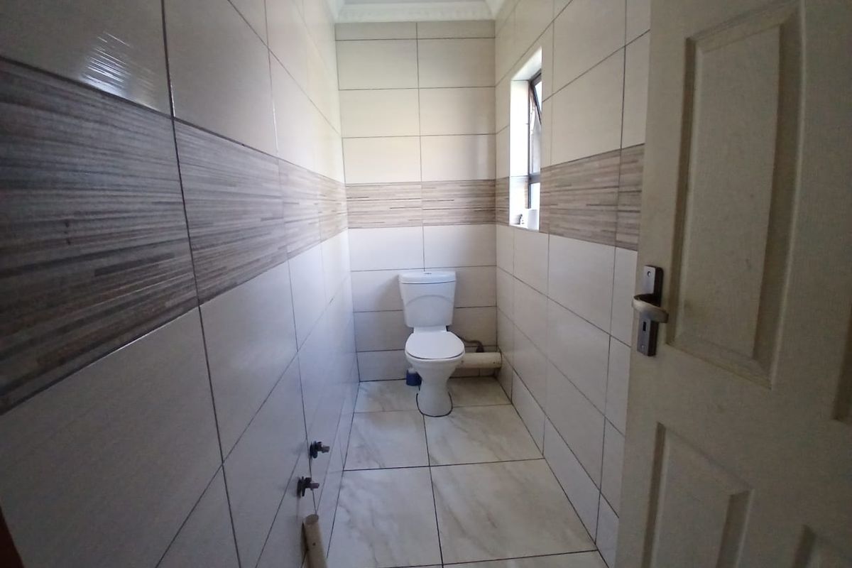 A compact bathroom featuring full-height wall tiling, floor tiles, and a standard toilet, with visible exposed plumbing requiring finishing.